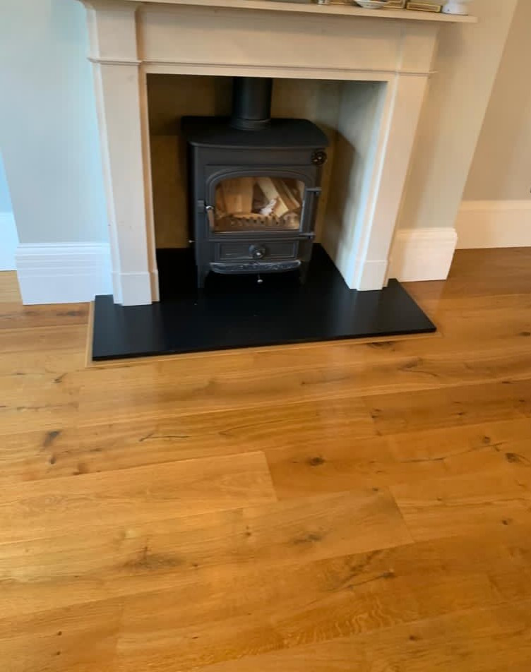 Photo of a mid-sized traditional enclosed living room in Hertfordshire with grey walls, medium hardwood floors, a wood stove, a plaster fireplace surround and brown floor.