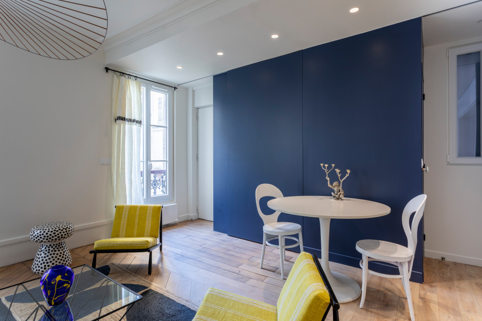 Modelo de sala de estar con biblioteca abierta contemporánea de tamaño medio sin chimenea con paredes azules, suelo de madera clara, suelo marrón y bandeja