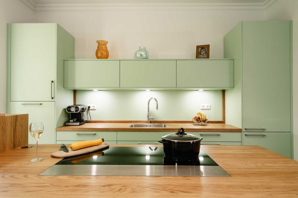 Mid-sized country open plan kitchen in Bremen with an undermount sink, flat-panel cabinets, green cabinets, wood benchtops, green splashback, black appliances, laminate floors, with island and grey floor.