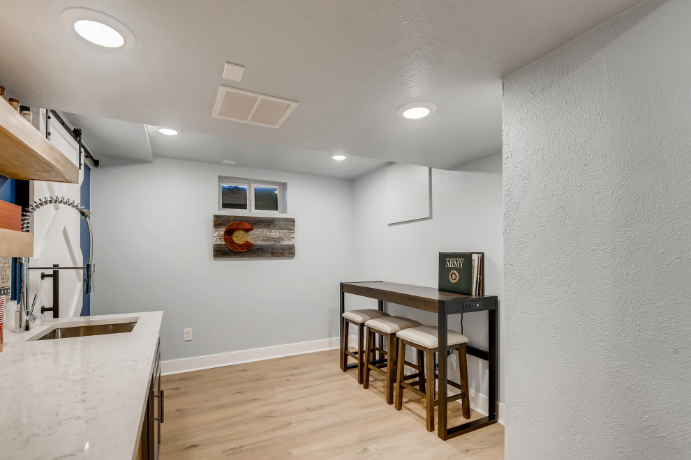 This is an example of a medium sized contemporary fully buried basement in Denver with a home bar, blue walls, vinyl flooring, brown floors and wallpapered walls.