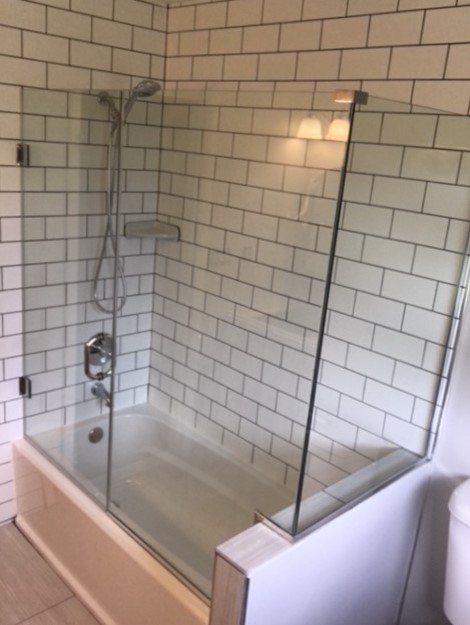 Photo of an industrial bathroom in DC Metro with a shower/bathtub combo, white tile, subway tile and a hinged shower door.