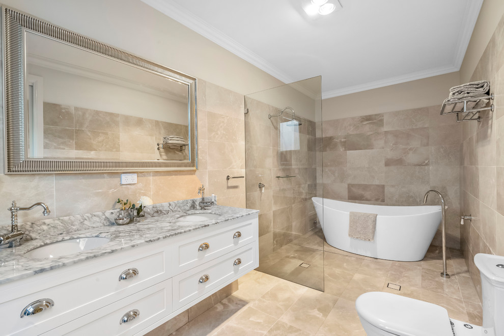 This is an example of a large contemporary master bathroom in Orange County with flat-panel cabinets, white cabinets, a freestanding tub, an open shower, beige tile, stone tile, a drop-in sink, marble benchtops, an open shower, white benchtops, a one-piece toilet, beige walls, slate floors and beige floor.