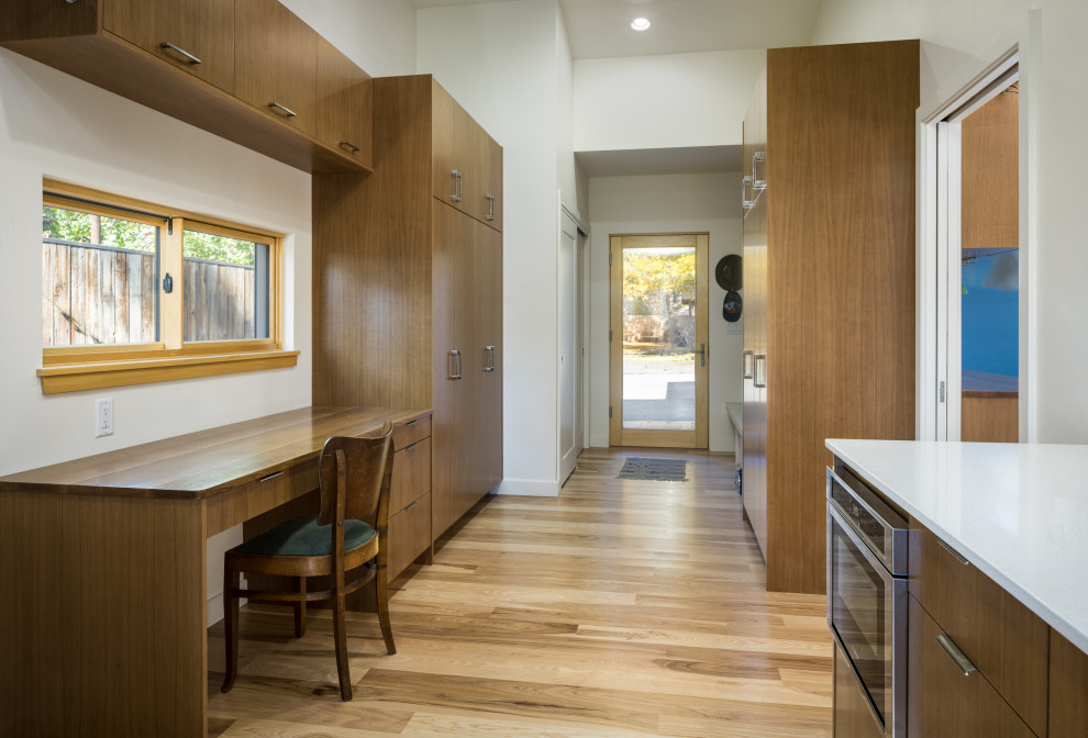 Photo of a mid-sized galley utility room in Other with flat-panel cabinets, medium wood cabinets, quartz benchtops, white walls, light hardwood floors, a side-by-side washer and dryer, white benchtop and vaulted.
