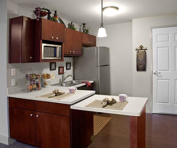 Inspiration for a small timeless l-shaped dark wood floor and brown floor enclosed kitchen remodel in Santa Barbara with a double-bowl sink, flat-panel cabinets, dark wood cabinets, quartz countertops, stainless steel appliances, a peninsula and white countertops