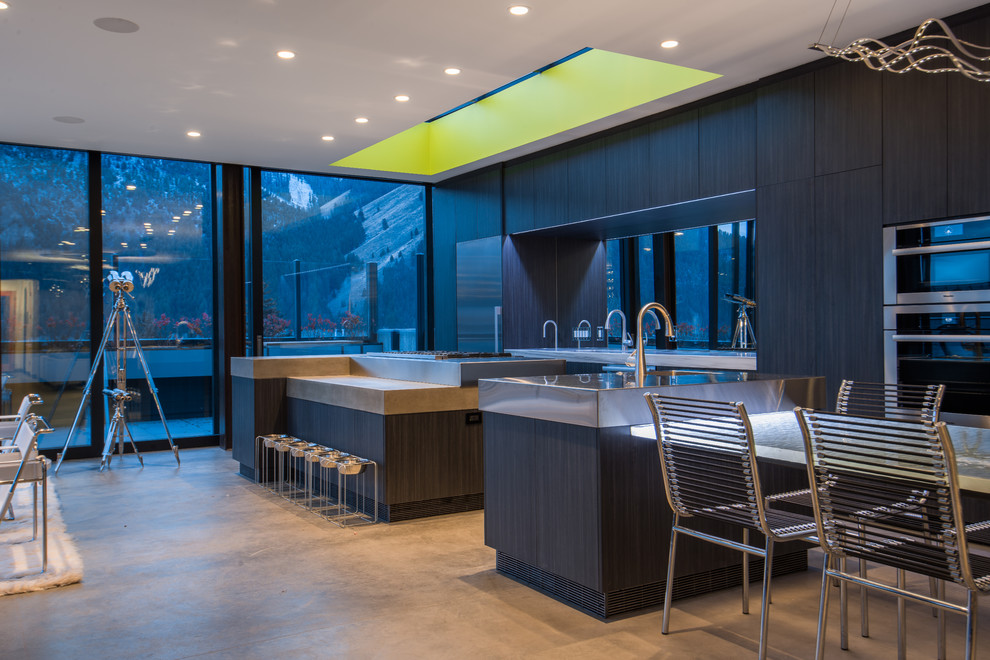 Modern galley open plan kitchen in Boise with an undermount sink, flat-panel cabinets, black cabinets, concrete benchtops, mirror splashback, stainless steel appliances, concrete floors and multiple islands.