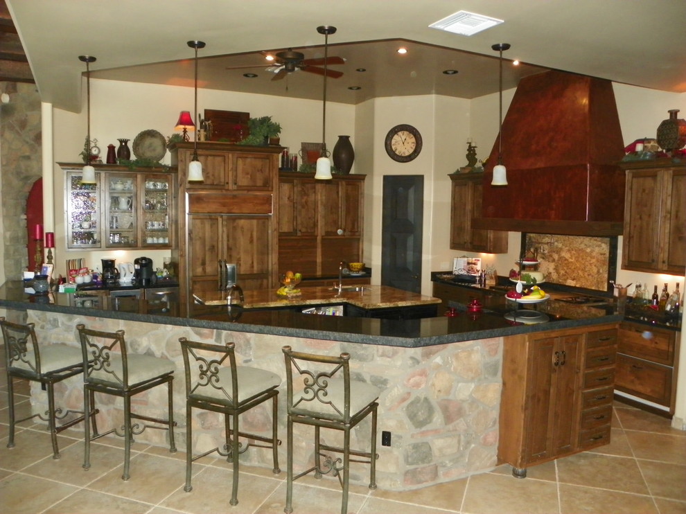 Eat-in kitchen - large mediterranean u-shaped travertine floor eat-in kitchen idea in Phoenix with a triple-bowl sink, raised-panel cabinets, distressed cabinets, granite countertops, brown backsplash, stone slab backsplash, stainless steel appliances and two islands
