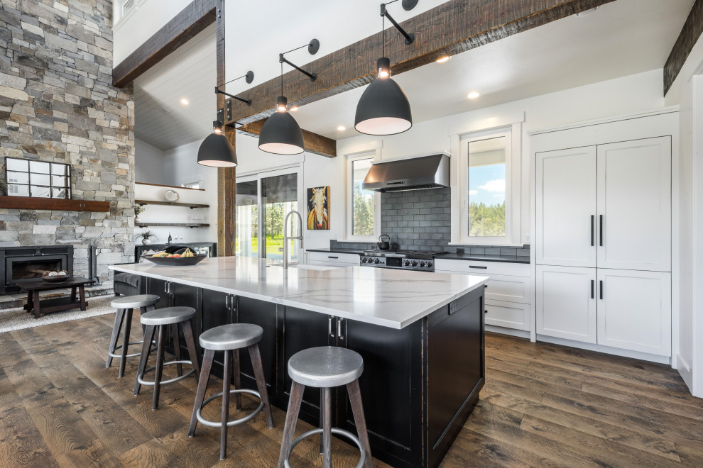 Design ideas for a country galley open plan kitchen in Boise with a farmhouse sink, ceramic splashback, medium hardwood floors, with island, brown floor, shaker cabinets, white cabinets, grey splashback, panelled appliances, black benchtop and exposed beam.