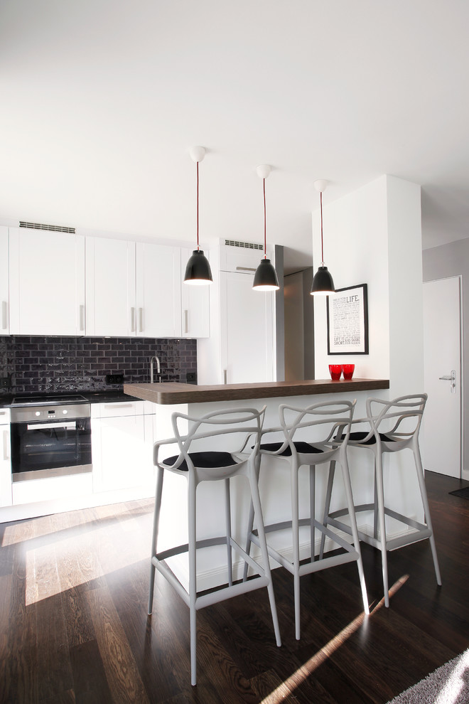 This is an example of a contemporary kitchen in Berlin with shaker cabinets, white cabinets, black splashback, subway tile splashback, panelled appliances, dark hardwood floors and a peninsula.