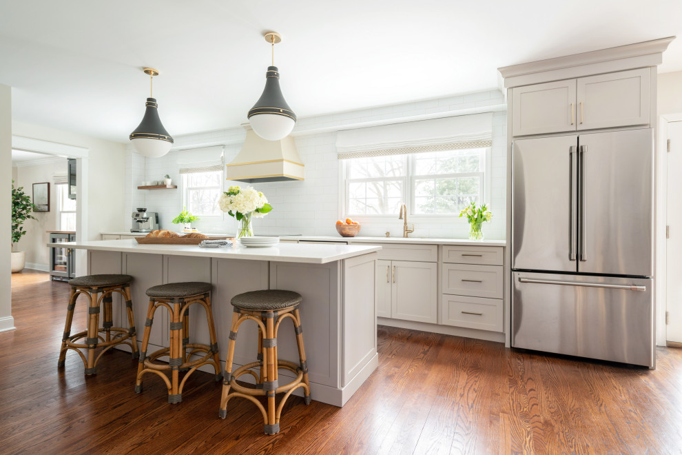 Photo of a large transitional galley eat-in kitchen in Philadelphia with a drop-in sink, shaker cabinets, beige cabinets, quartz benchtops, white splashback, cement tile splashback, stainless steel appliances, dark hardwood floors, with island and white benchtop.