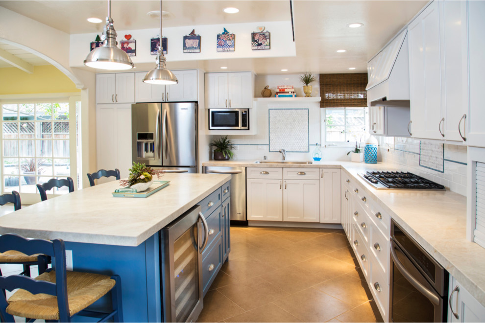 This is an example of a mid-sized transitional l-shaped open plan kitchen in San Diego with a single-bowl sink, shaker cabinets, white cabinets, white splashback, subway tile splashback, with island, quartz benchtops, stainless steel appliances and porcelain floors.