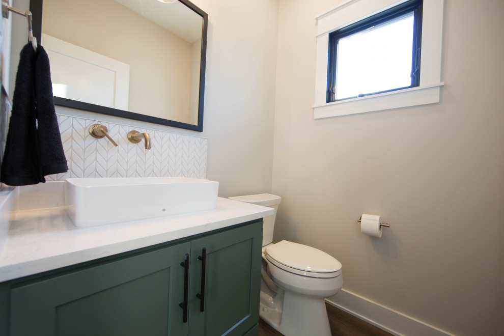 This is an example of a small contemporary cloakroom in Indianapolis with recessed-panel cabinets, grey cabinets, a two-piece toilet, white tiles, porcelain tiles, beige walls, laminate floors, a vessel sink, quartz worktops, brown floors, white worktops and a freestanding vanity unit.