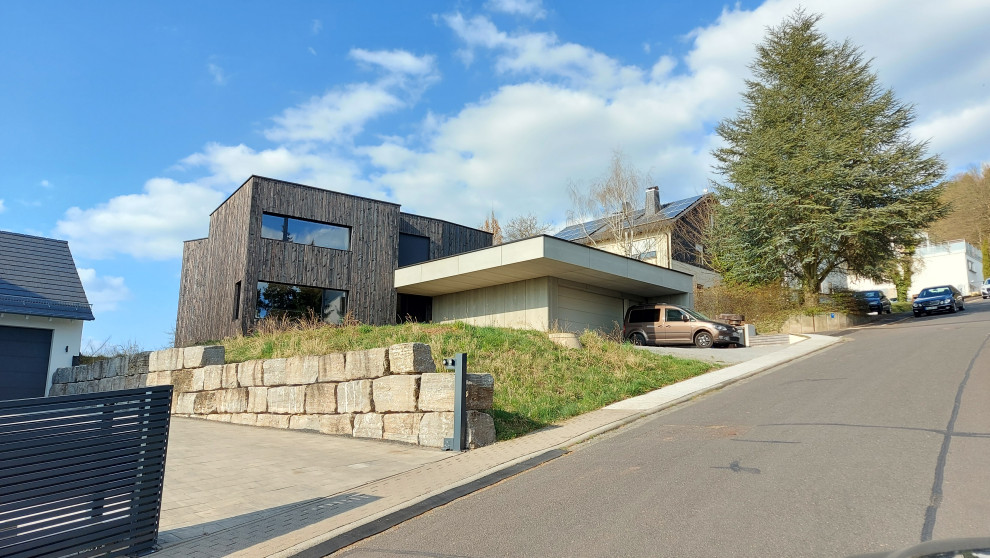 Стильный дизайн: огромный, двухэтажный, деревянный, черный частный загородный дом в современном стиле с плоской крышей, зеленой крышей и отделкой планкеном - последний тренд