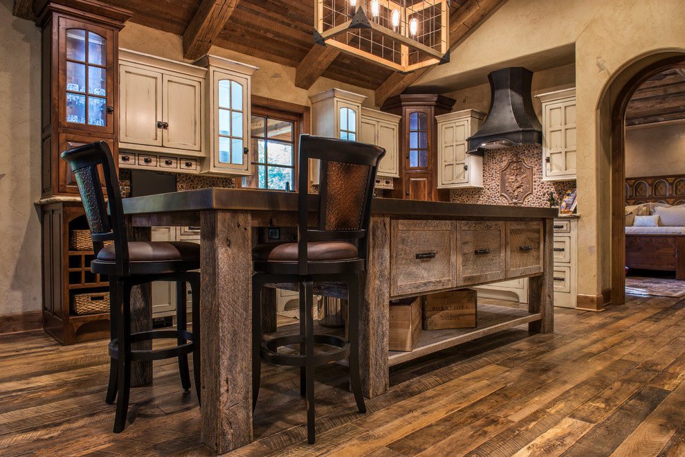 Example of a large mountain style u-shaped dark wood floor enclosed kitchen design with recessed-panel cabinets, distressed cabinets, granite countertops, an island, a farmhouse sink, brown backsplash and paneled appliances