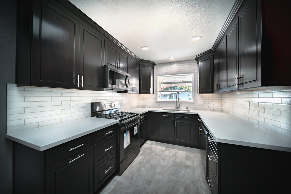 This is an example of a mid-sized modern u-shaped kitchen in Sacramento with a double-bowl sink, beaded inset cabinets, black cabinets, quartzite benchtops, white splashback, ceramic splashback, stainless steel appliances, no island, white floor and white benchtop.