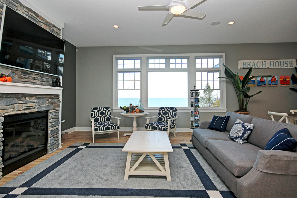 This is an example of a beach style formal open concept living room in Grand Rapids with grey walls, light hardwood floors, a standard fireplace, a stone fireplace surround and a wall-mounted tv.
