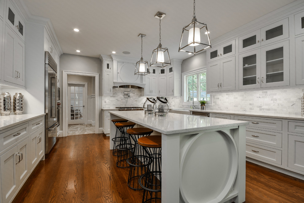 Photo of a large transitional u-shaped eat-in kitchen in Boston with a farmhouse sink, beaded inset cabinets, white cabinets, quartz benchtops, white splashback, marble splashback, stainless steel appliances, dark hardwood floors, with island and brown floor.