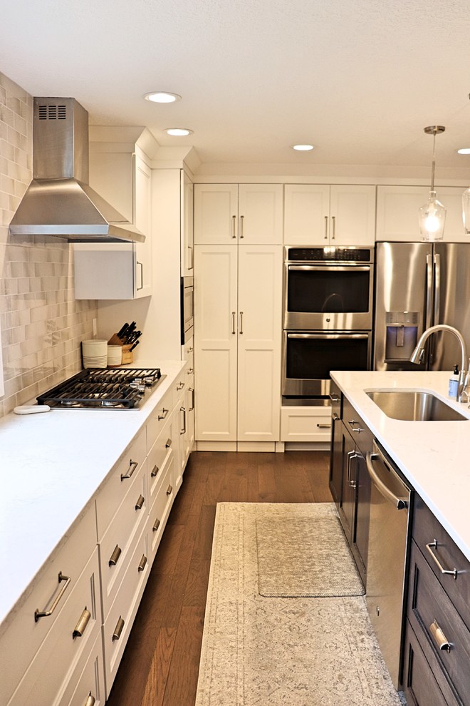 Inspiration for a large transitional l-shaped medium tone wood floor and brown floor kitchen pantry remodel in Cedar Rapids with an undermount sink, recessed-panel cabinets, white cabinets, quartzite countertops, gray backsplash, porcelain backsplash, stainless steel appliances, an island and white countertops