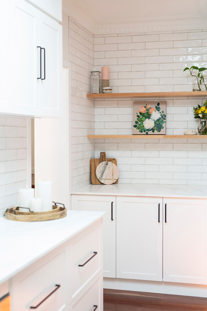 Foto på ett mellanstort industriellt vit kök, med en undermonterad diskho, skåp i shakerstil, vita skåp, bänkskiva i kvarts, vitt stänkskydd, stänkskydd i tunnelbanekakel, rostfria vitvaror, mörkt trägolv och en köksö