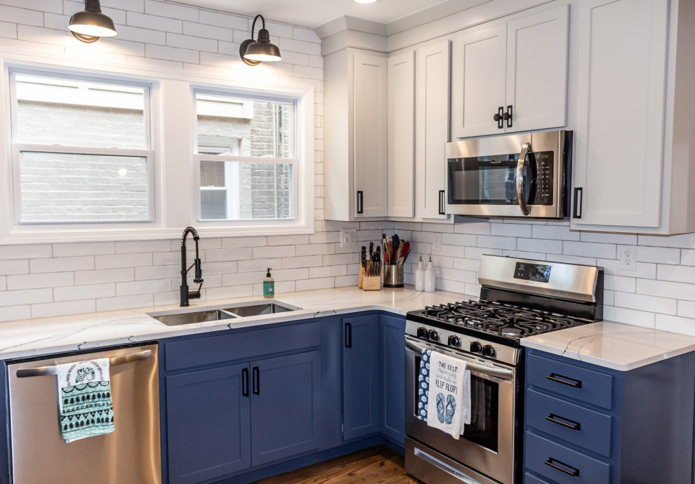 Small transitional u-shaped eat-in kitchen in St Louis with an undermount sink, shaker cabinets, blue cabinets, quartz benchtops, white splashback, subway tile splashback, stainless steel appliances, medium hardwood floors, brown floor and white benchtop.