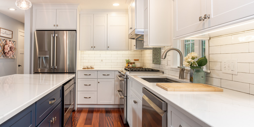 Photo of a mid-sized contemporary l-shaped eat-in kitchen in Portland Maine with an undermount sink, shaker cabinets, white cabinets, quartz benchtops, white splashback, subway tile splashback, stainless steel appliances, medium hardwood floors, with island, red floor and white benchtop.