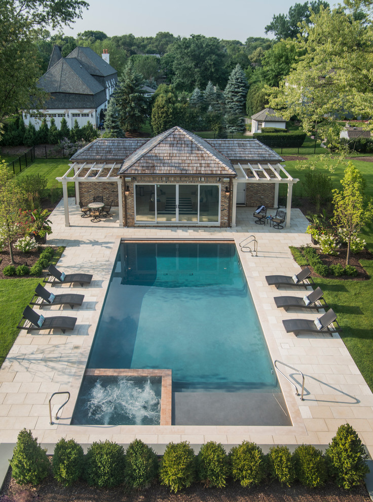 This is an example of a mid-sized traditional backyard rectangular lap pool in Chicago with a hot tub and natural stone pavers.