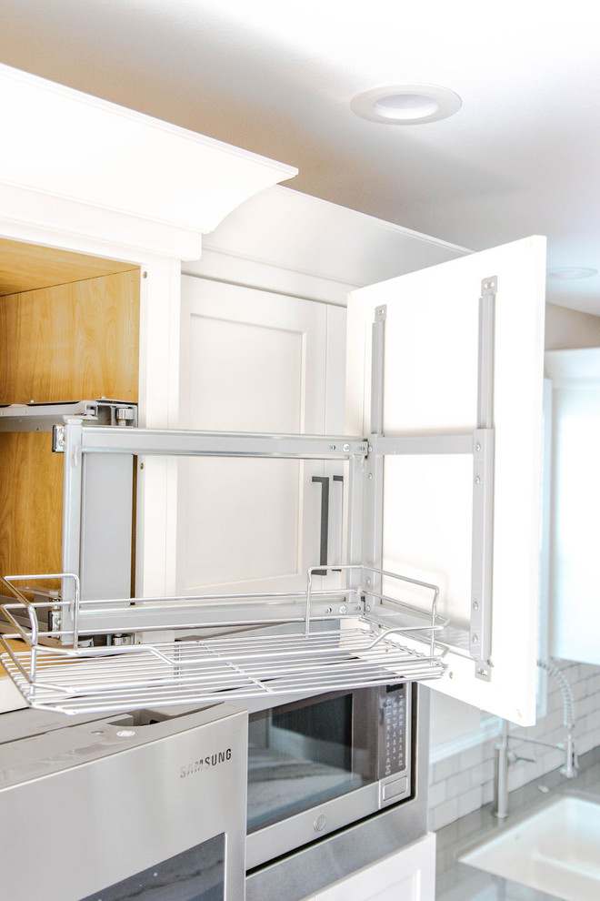Inspiration for a mid-sized transitional l-shaped medium tone wood floor and brown floor eat-in kitchen remodel in Omaha with a farmhouse sink, shaker cabinets, white cabinets, quartzite countertops, white backsplash, subway tile backsplash, stainless steel appliances, an island and white countertops