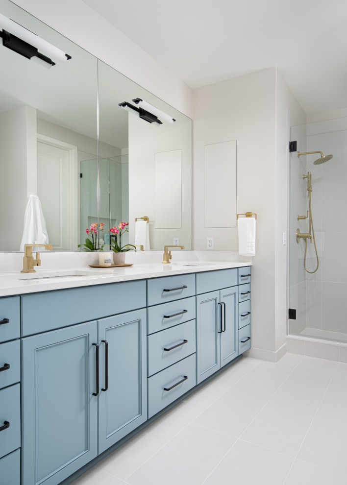 Photo of a large transitional bathroom in Kansas City with recessed-panel cabinets, blue cabinets, an alcove shower, beige tile, porcelain tile, beige walls, porcelain floors, an undermount sink, engineered quartz benchtops, beige floor, a hinged shower door, white benchtops, a double vanity and a built-in vanity.