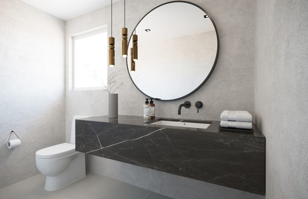 Mid-sized modern powder room in Montreal with a one-piece toilet, beige walls, porcelain floors, an undermount sink, marble benchtops, grey floor and grey benchtops.