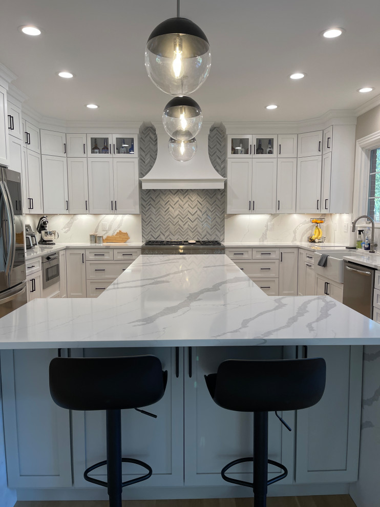 Eat-in kitchen - large contemporary u-shaped light wood floor and beige floor eat-in kitchen idea with a farmhouse sink, shaker cabinets, white cabinets, quartz countertops, gray backsplash, quartz backsplash, stainless steel appliances, an island and white countertops