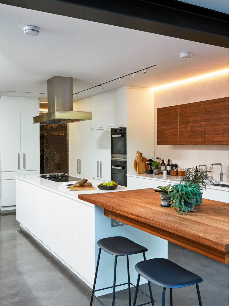 Photo of a contemporary l-shaped kitchen in London with an undermount sink, flat-panel cabinets, white cabinets, stainless steel appliances, concrete floors, with island, grey floor and white benchtop.