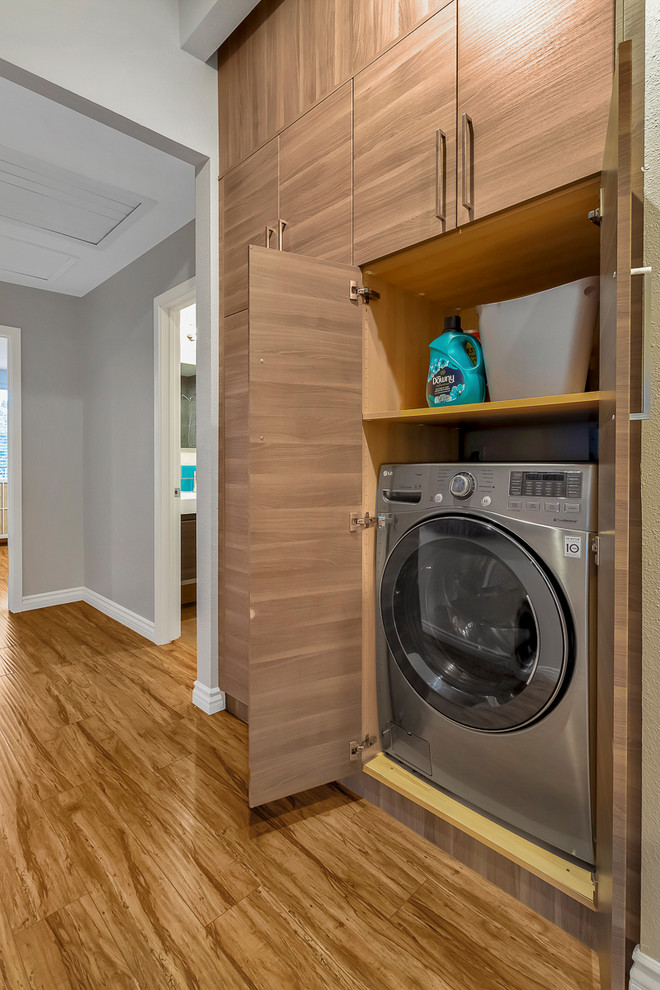 Small contemporary galley laundry cupboard in Los Angeles with flat-panel cabinets, medium wood cabinets, grey walls, light hardwood floors, a side-by-side washer and dryer and brown floor.