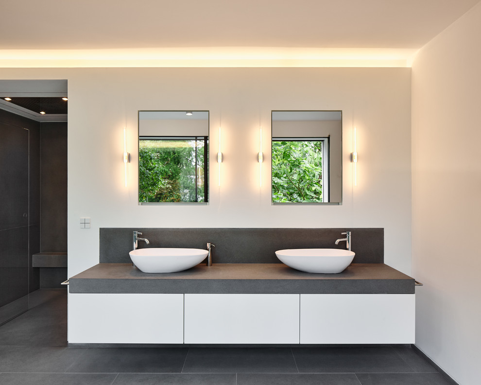 Inspiration for an expansive contemporary master bathroom in Cologne with a vessel sink, a freestanding tub, flat-panel cabinets, white cabinets, gray tile, stone tile, white walls and solid surface benchtops.