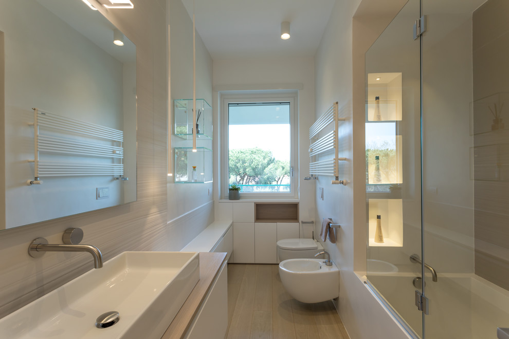 This is an example of a contemporary bathroom in Rome with flat-panel cabinets, white cabinets, a corner tub, a shower/bathtub combo, a bidet, white walls, a drop-in sink, wood benchtops, beige floor, a hinged shower door and beige benchtops.