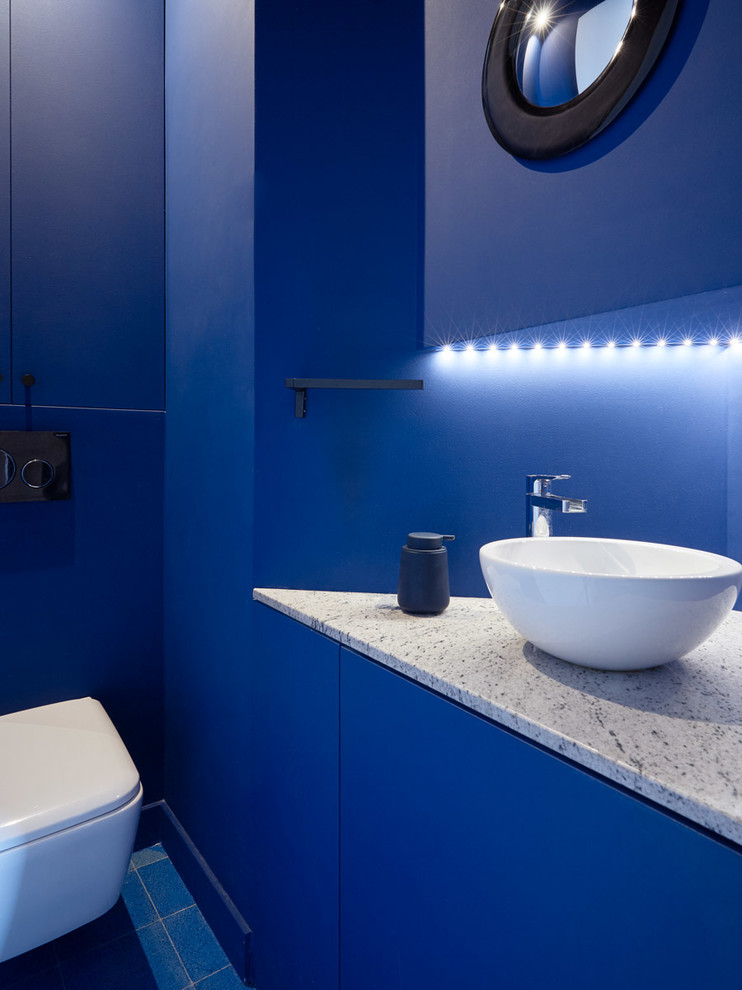 This is an example of a contemporary powder room in Paris with flat-panel cabinets, blue cabinets, a wall-mount toilet, blue walls, a vessel sink, blue floor and grey benchtops.
