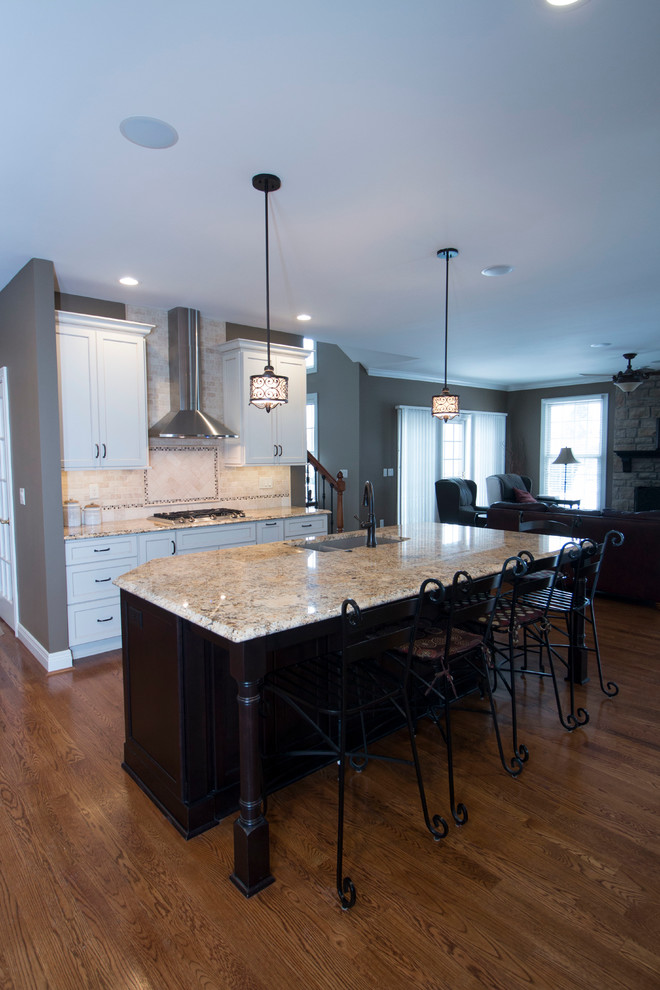 This is an example of a large traditional l-shaped eat-in kitchen in Cincinnati with an undermount sink, shaker cabinets, white cabinets, granite benchtops, beige splashback, stone tile splashback, stainless steel appliances, medium hardwood floors and with island.