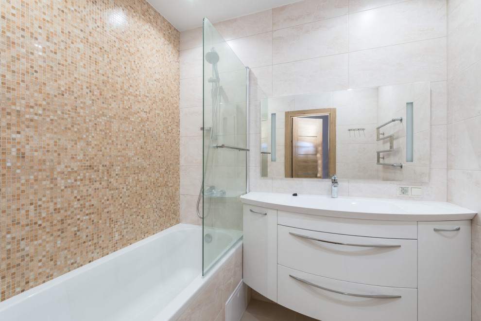 Inredning av ett modernt mellanstort en-suite badrum, med släta luckor, vita skåp, ett badkar i en alkov, en dusch/badkar-kombination, en vägghängd toalettstol, beige kakel, beige väggar, klinkergolv i keramik, ett integrerad handfat och beiget golv