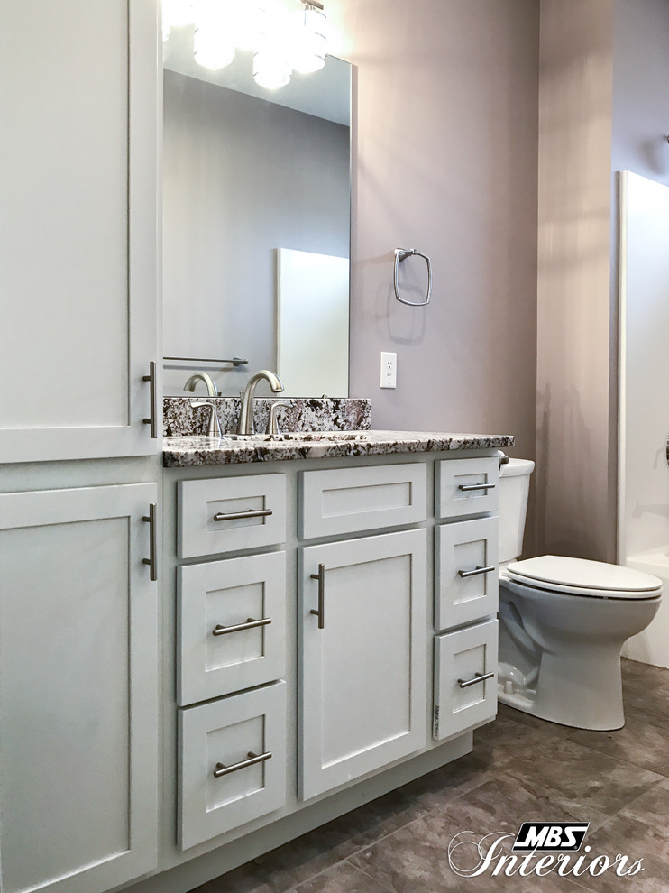 Inspiration for a mid-sized arts and crafts master bathroom in Other with shaker cabinets, white cabinets, a drop-in tub, a shower/bathtub combo, a one-piece toilet, gray tile, ceramic tile, purple walls, ceramic floors, an undermount sink, granite benchtops, grey floor and a shower curtain.