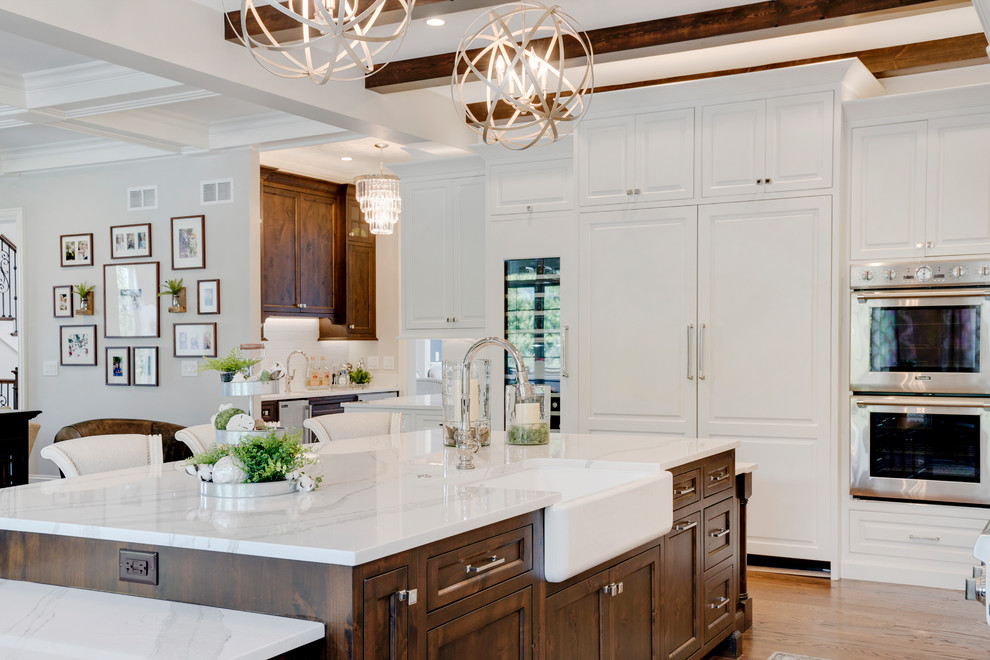Traditional open plan kitchen in Chicago with a farmhouse sink, recessed-panel cabinets, dark wood cabinets, quartz benchtops, panelled appliances, medium hardwood floors, with island, brown floor and white benchtop.
