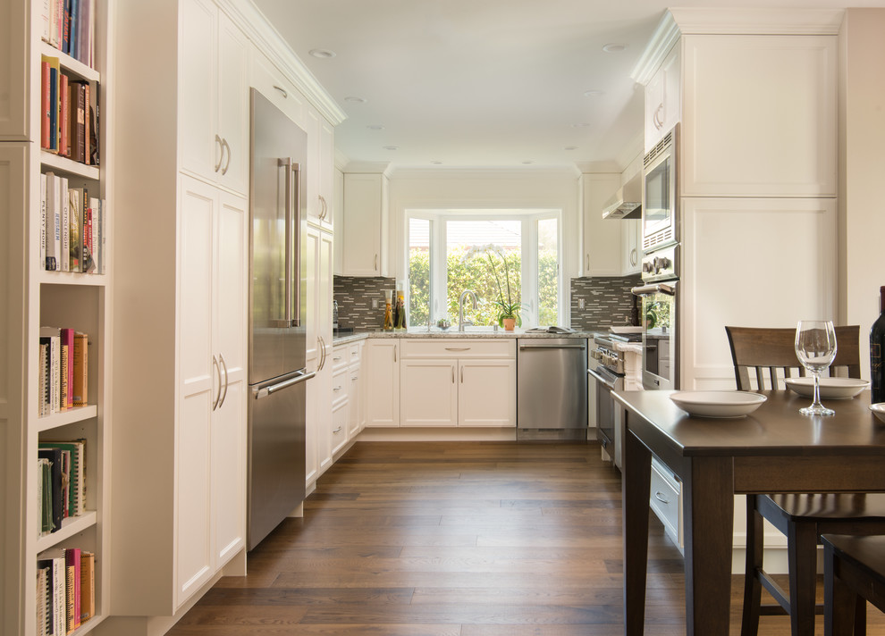 Example of a mid-sized transitional u-shaped dark wood floor eat-in kitchen design in Los Angeles with an undermount sink, raised-panel cabinets, white cabinets, granite countertops, gray backsplash, matchstick tile backsplash and stainless steel appliances