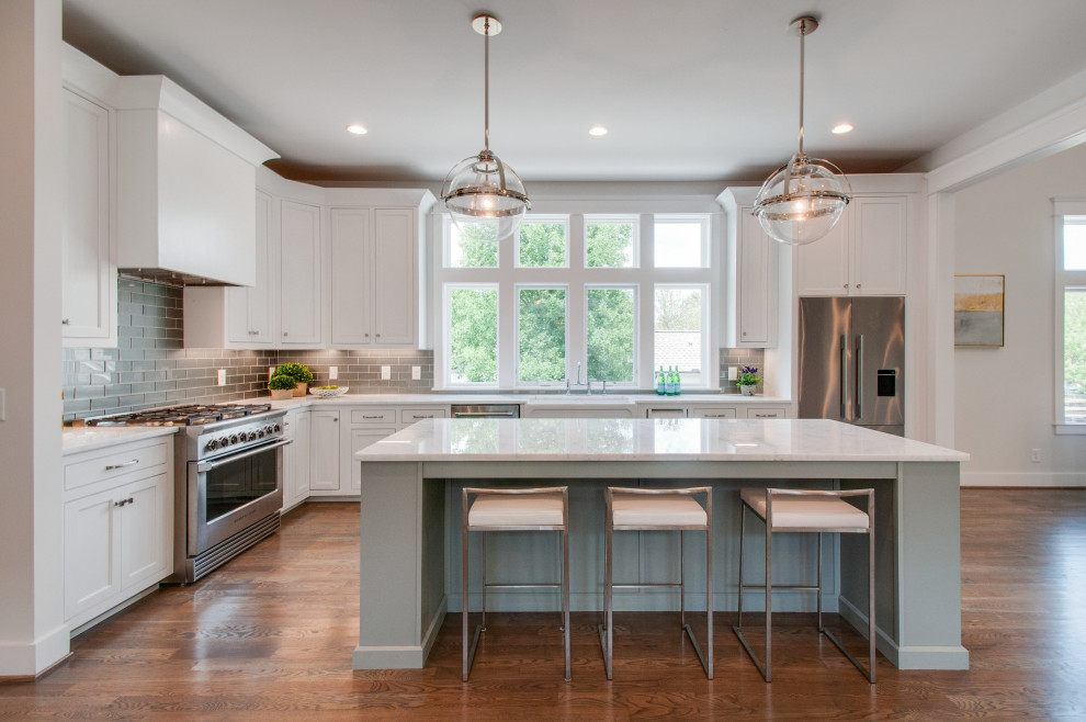 Design ideas for a large transitional l-shaped eat-in kitchen in Nashville with a farmhouse sink, recessed-panel cabinets, white cabinets, quartz benchtops, grey splashback, glass tile splashback, stainless steel appliances, medium hardwood floors, with island, white benchtop and brown floor.