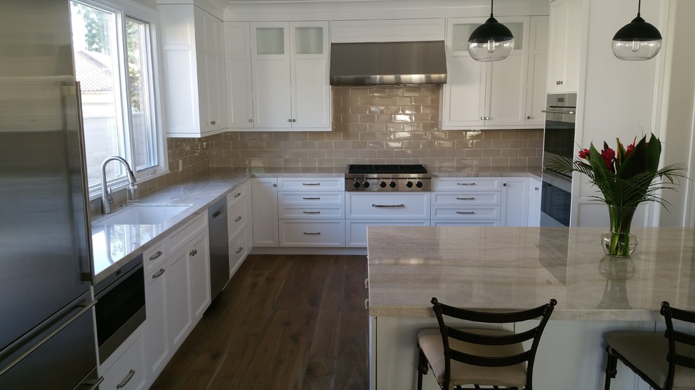 Inspiration for a mid-sized transitional u-shaped dark wood floor and brown floor eat-in kitchen remodel in Orange County with an undermount sink, recessed-panel cabinets, white cabinets, limestone countertops, gray backsplash, subway tile backsplash, stainless steel appliances, a peninsula and beige countertops
