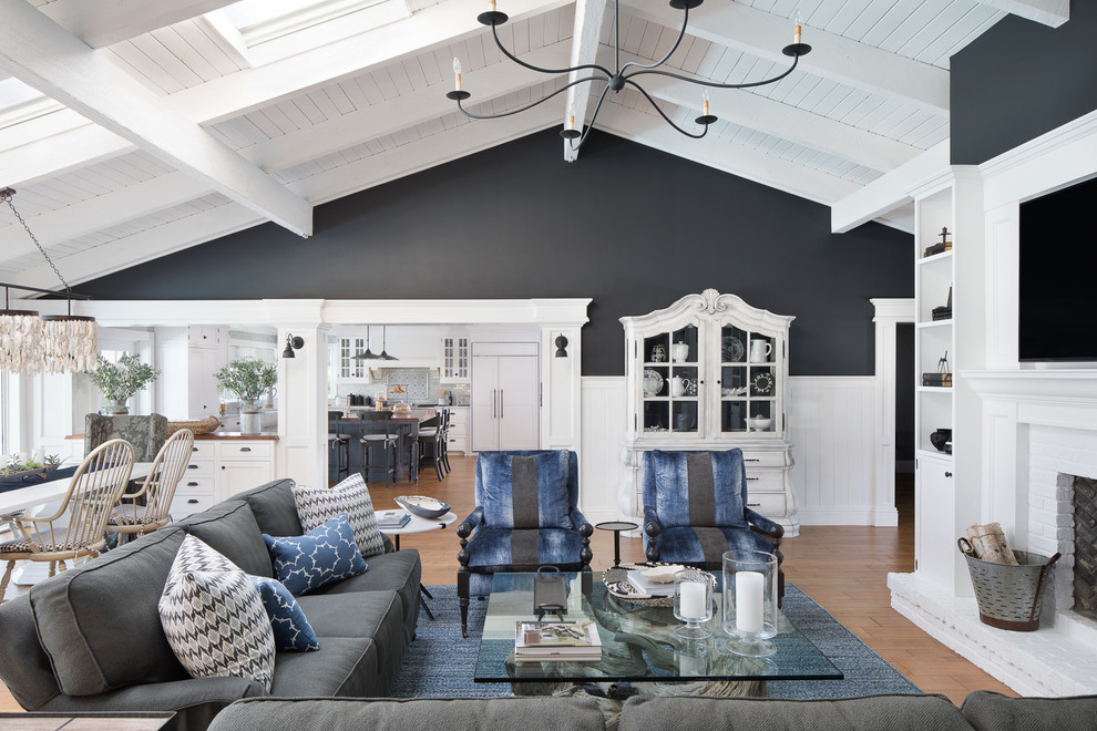 Inspiration for a large coastal open concept medium tone wood floor and brown floor family room remodel in Miami with black walls, a standard fireplace, a brick fireplace and a wall-mounted tv