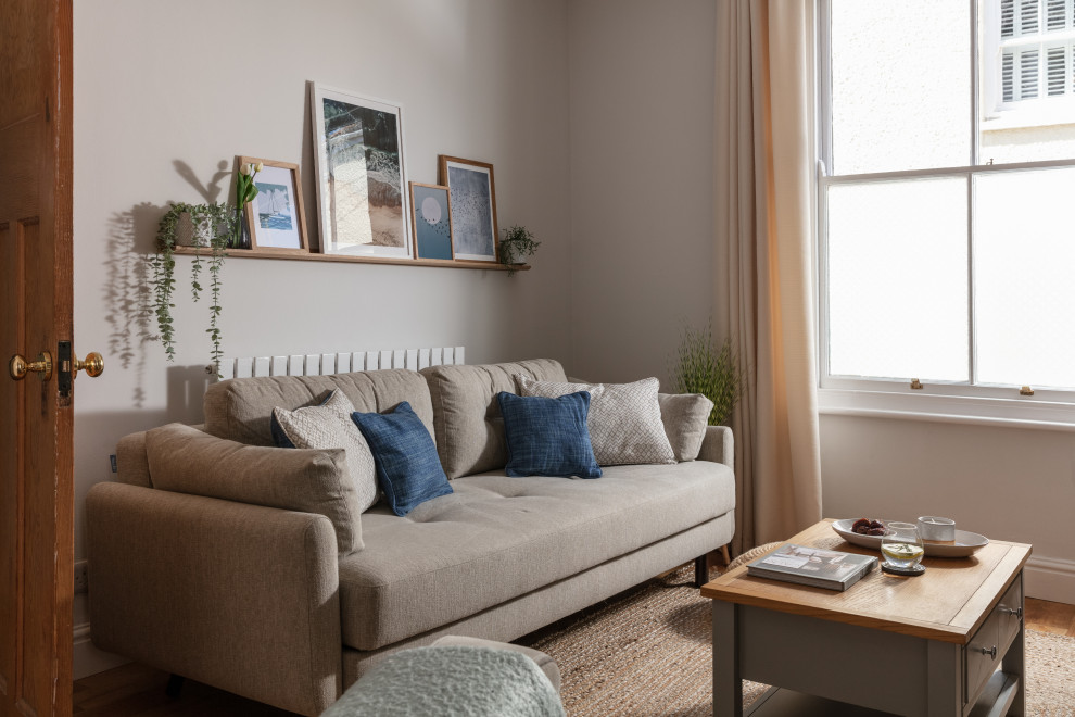 Mittelgroßes, Repräsentatives, Offenes Nordisches Wohnzimmer mit grauer Wandfarbe, braunem Holzboden, Eck-TV und braunem Boden in Cornwall