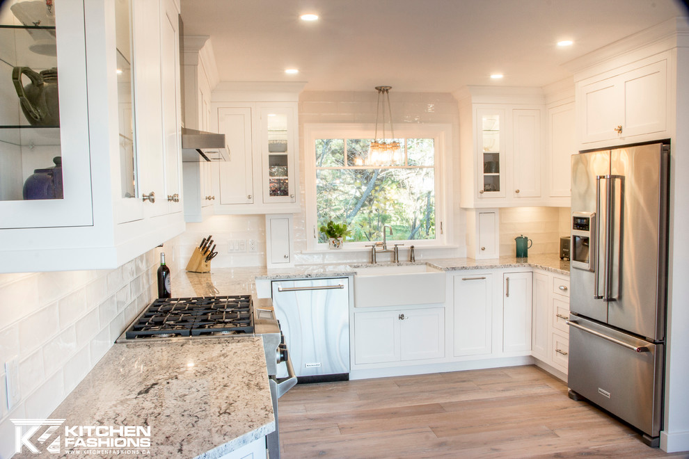 Eat-in kitchen - large transitional u-shaped light wood floor eat-in kitchen idea with a farmhouse sink, shaker cabinets, white cabinets, granite countertops, white backsplash, subway tile backsplash, stainless steel appliances and no island