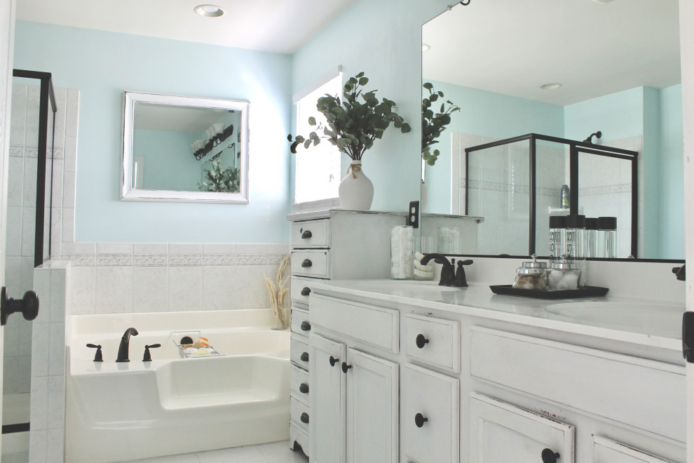 This is an example of a mid-sized traditional master bathroom in Charlotte with raised-panel cabinets, white cabinets, a drop-in tub, an alcove shower, a one-piece toilet, multi-coloured tile, ceramic tile, white walls, ceramic floors, an integrated sink, quartzite benchtops, white floor, a hinged shower door, white benchtops, an enclosed toilet, a double vanity and a built-in vanity.