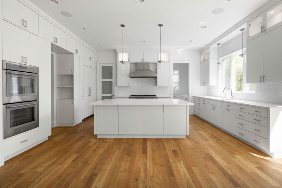Klassisk inredning av ett vit vitt kök, med en undermonterad diskho, släta luckor, vita skåp, bänkskiva i kvarts, vitt stänkskydd, stänkskydd i keramik, integrerade vitvaror, mellanmörkt trägolv och en köksö