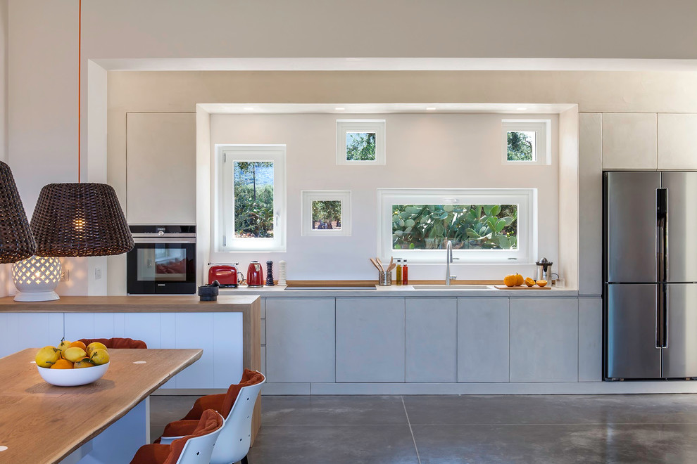 Expansive modern single-wall open plan kitchen in Other with an integrated sink, beaded inset cabinets, concrete benchtops, beige splashback, window splashback, concrete floors, a peninsula, grey floor and beige benchtop.