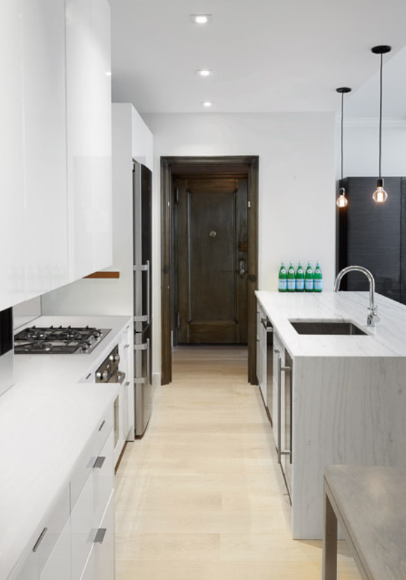 Photo of a small industrial galley eat-in kitchen in New York with an undermount sink, flat-panel cabinets, white cabinets, stainless steel appliances, with island, beige floor and light hardwood floors.