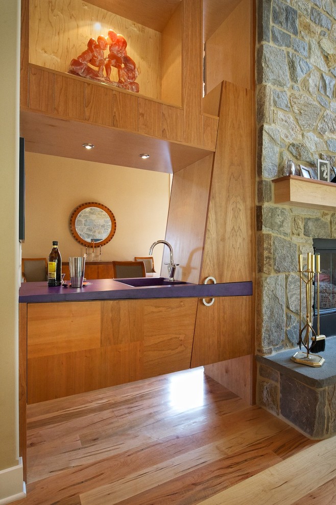This is an example of a small modern single-wall wet bar in Philadelphia with an integrated sink, flat-panel cabinets, light wood cabinets, solid surface benchtops, light hardwood floors and purple benchtop.