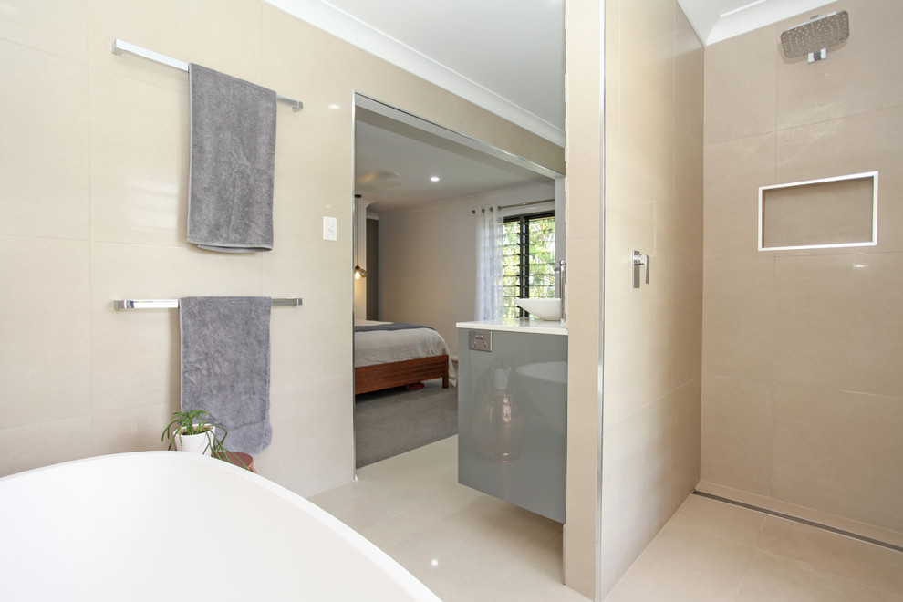 This is an example of a large beach style master bathroom with flat-panel cabinets, grey cabinets, a freestanding tub, a curbless shower, a one-piece toilet, white tile, porcelain tile, beige walls, porcelain floors, a vessel sink, engineered quartz benchtops, beige floor and an open shower.